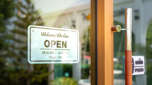Open welcome sign in white color which is hanging at the glass front door of coffee shop. Sign and symbol for busines, close-up and selective focus.