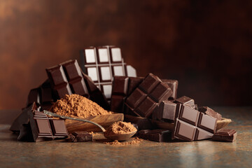 Scraps of dark chocolate next to a wooden bowl of cocoa powder.