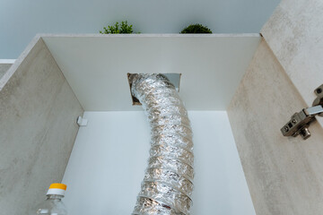 A long hose is protruding from an opening that is situated in the wall of a cabinet, and this might...