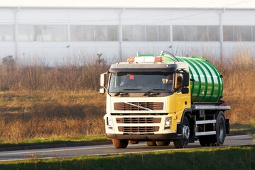 Yellow liquid waste truck on countryside road by industrial area