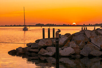 Sailboat approaching harbor entrance of Wiek at sunset over Wiek Bodden lagoon, Rügen, Mecklenburg-Vorpommern, Germany