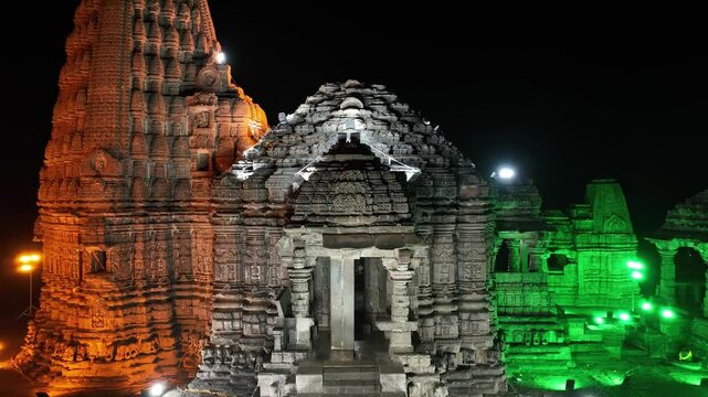 aerial night view of Gondeshwar Hindu temple of India illuminated in the colors of Indian flag: orange, white, green. saffron flag flies atop. stonework of temple is highlighted by strategic lighting