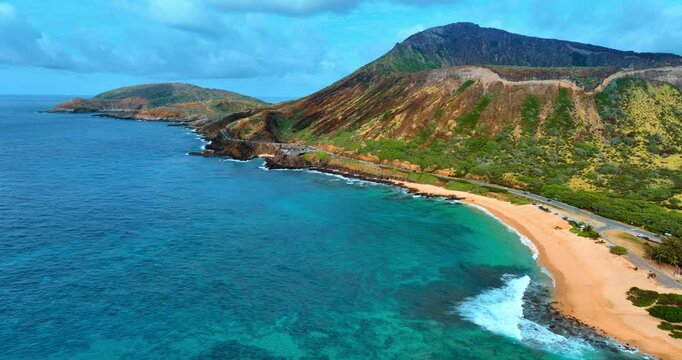 Foamy waves arrive to the sandy beach at the picturesque mountains of the Oahu Island, Hawaii, USA. Footage along the stunning rocks at the coastline. Aerial perspective.