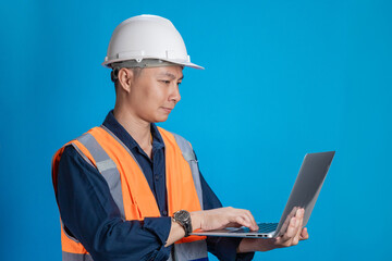 Confident young engineer wearing orange and a safety helmet stands holding a laptop, phone with various emotions.