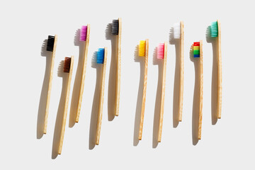 Eco friendly Bamboo toothbrushes with colored bristles at sunlight with dark shadows on white background. Sustainable living concepts, minimal style aesthetic photo, top view set wood oral brushes