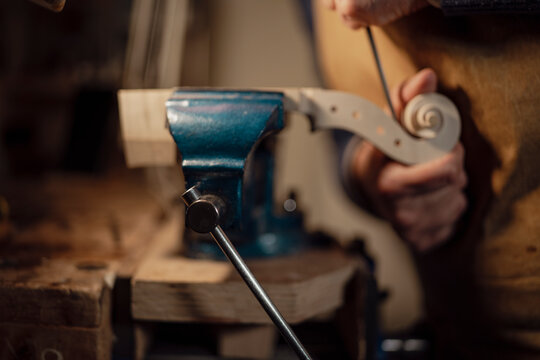 Skilled luthier carefully carving violin scroll, hands working intricate wood details with precision in traditional workshop setting