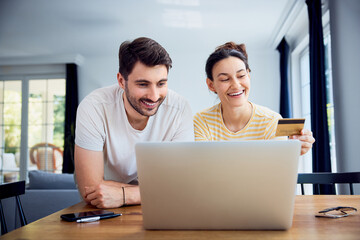 Obraz premium Young couple paying with credit card for online shoping using laptop at home