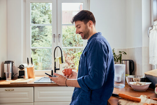 Man using mobile phone while having coffee in kitchen