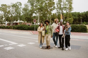 Obraz premium A young Black man in his late 20s, smiling as he walks across the road with his young Latina girlfriend by his side and their three adult friends next to them, on a city street