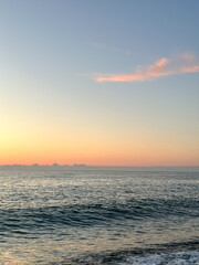 ocean sunset reveal, tranquil sunset ocean view with gentle waves, clear sky, and soft peach-to-blue horizon meets a hint of pink cloud