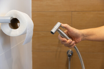 Woman is holding a stainless steel handheld bidet sprayer in bathroom.