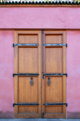 A wooden door with a gold handle and a black bolt. The door is open. The door is on a pink wall