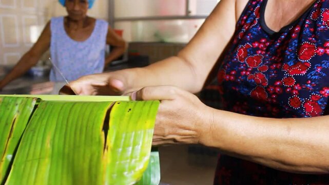 An unrecognizable person's hands cutting a banana leaf to prepare Quesillo inside a kitchen in Yaguara, Huila, Colombia. Colombian food concept