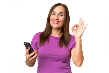 Middle-aged caucasian woman over isolated background using mobile phone and doing OK sign