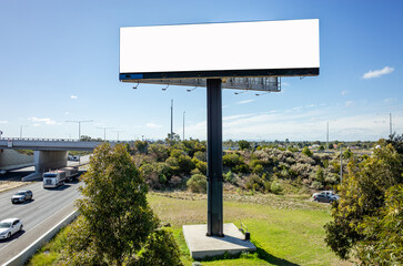 Background texture of a large blank white mockup billboard on a tall support pillar, positioned next to a highway with busy traffic. Copy space for commercial advertisement design.