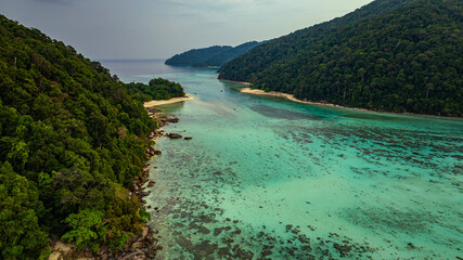 Fototapeta premium A stunning aerial view of lush green tropical islands surrounded by crystal-clear turquoise waters. The coral reefs and sandy shores contrast beautifully against the deep blue ocean. Surin Islands