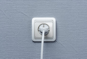 A white European-style electrical socket with a plug inserted, mounted on a textured light gray...