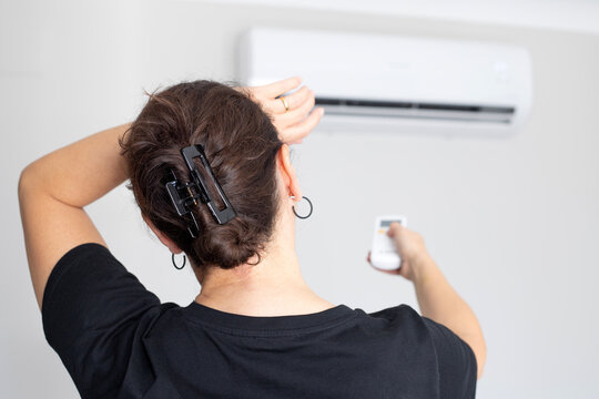 A woman, feeling the heat, reaches up to activate her air conditioner with a remote control for a cool environment.
