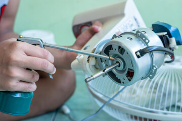A man is cleaning a fan, including cleaning the propeller, the engine (and providing lubricants), and cleaning the fan guard grill