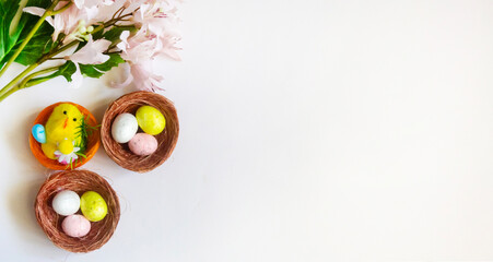 Colorful Easter eggs in a basket on a light background, next to a branch with flowers. There is a place for copying.