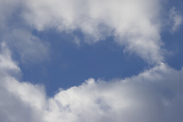 Obraz premium blue sky framed with gray clouds, large gray clouds, a few blue patches of sky are visible, grey passing clouds and a few blue spots, white fluff in the sky, grey haze accumulation