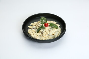 Creamy pasta in black bowl: penne with white sauce, herbs, cheese, and a tomato on a white background