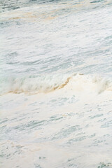 The white foam of the ocean crashing against the shore, creating dynamic patterns as the waves break. The foam contrasts with the deep blue of the water, adding texture and movement to the seascape
