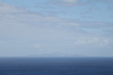 Fototapeta premium Misty ocean view with a distant island barely visible through the thick fog. Calm and moody atmosphere with soft, diffused light over the water.