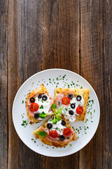 Pinsa Romana with mortadella, burrata cheese, black olives and cherry tomatoes on wooden table	