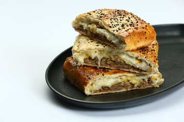 Stacked, sliced Stromboli on black plate: filled with meat and/or sausage and cheese on white