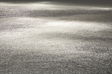 A breathtaking view of the ocean shimmering in silver tones as it reflects the sunlight. The surface sparkles with a metallic sheen, creating a serene, luminous seascape that radiates peace