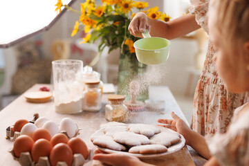 Kids baking cookies together, dusting flour in cozy kitchen with eggs and ingredients on the table.