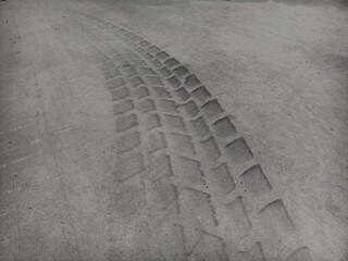 Black and white photography depicting a tire track imprinted on a rough concrete surface