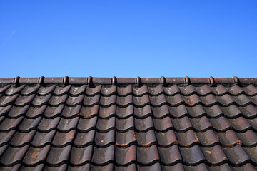 A close-up of a roof with brown ceramic tiles against a clear blue sky, showing the texture and detail of the roof's surface
