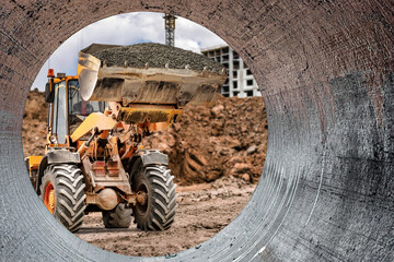 Construction worker operates loader to move materials into pipe at construction site during day