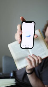 Vertical screen multitasking moment guy holds up book and phone with ChatGPT like cross-referencing ancient wisdom with modern AI brain academic vibes study mode activated