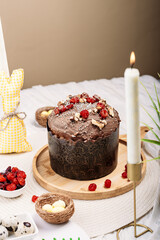 Easter Easter cake, Easter bread with chocolate glaze decorated with dried cherries and walnuts on a light background, tall candles, flowers, Easter bunny nearby. Easter concept