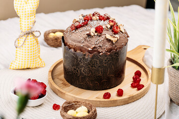 Easter Easter cake, Easter bread with chocolate glaze decorated with dried cherries and walnuts on a light background, tall candles, flowers, Easter bunny nearby. Easter concept