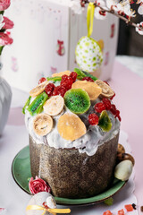 Easter Easter cake, Easter bread decorated with dried fruits: figs, dried apricots, raisins, candied fruits, kiwi. Easter bread tied with a pink ribbon on a light background next to flowers.