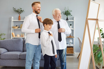 Obraz premium Family connection. Three generations of men are gathered in front of mirror, each dressed in white shirt and black tie. Grandfather, father and grandson are smiling while trying on identical clothes.
