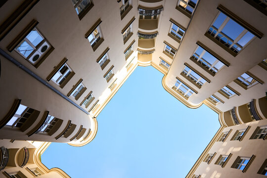 Architectural upward shot of a symmetrical inner courtyard with curved building edges and classical windows, captured in natural daylight against a clear blue sky.