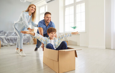 Happy family couple with child boy on moving day having fun in new apartment riding son in...