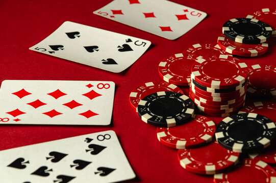 A group of two pairs playing cards and poker chips are arranged on a red table, creating an atmosphere of excitement during a friendly gaming evening. A good or lucky win at poker
