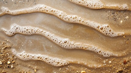 Obraz premium Close-Up View of Gentle Waves Rolling Over Golden Sand with Seafoam and Pebbles on a Tranquil Beach