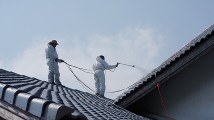 House painter standing on roof spray painting