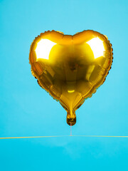 Close up of golden inflated heart shaped balloon for entertainment and party on blue background