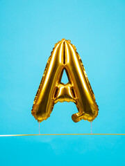 Close up of golden inflated letter A shaped balloon for entertainment and party on blue background