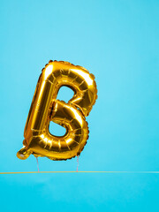 Close up of golden inflated balloon in the shape of letter B for entertainment and parties on blue...
