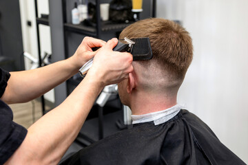 Hairdresser cutting hair of young man in barbershop, closeup shot