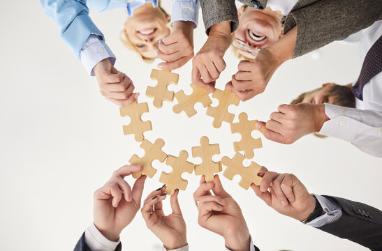 Bottom view of happy united diverse group of business people standing in circle and stacking wooden jigsaw puzzle together during team building activity. Unity, teamwork and collaboration concept.